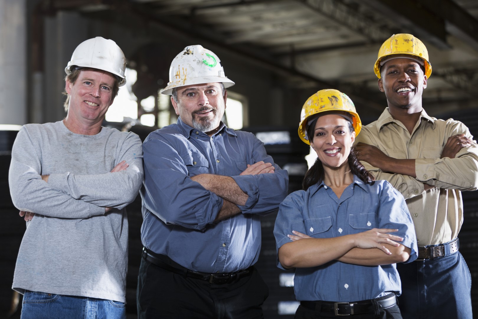 Diverse group of 4 smiling construction workers standing next to one another with their arms crossed